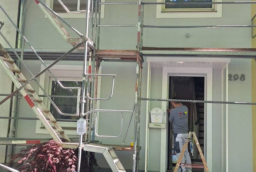 Ein Baugerüst an einer grünen Hauswand unter dem Handerker und Trockenbauer Christian Effertz durchgeht